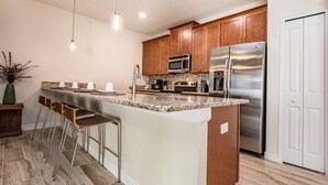 A modern kitchen with granite countertops, stainless steel appliances, wooden cabinets, and a bar area with stools. - 4bed 3Ba Champions Gate Pool Home (Davenport)