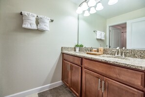 A bathroom with a granite countertop, wooden cabinets, a large mirror, and two towels hanging on the wall. - 4bed 3Ba Champions Gate Pool Home (Davenport)