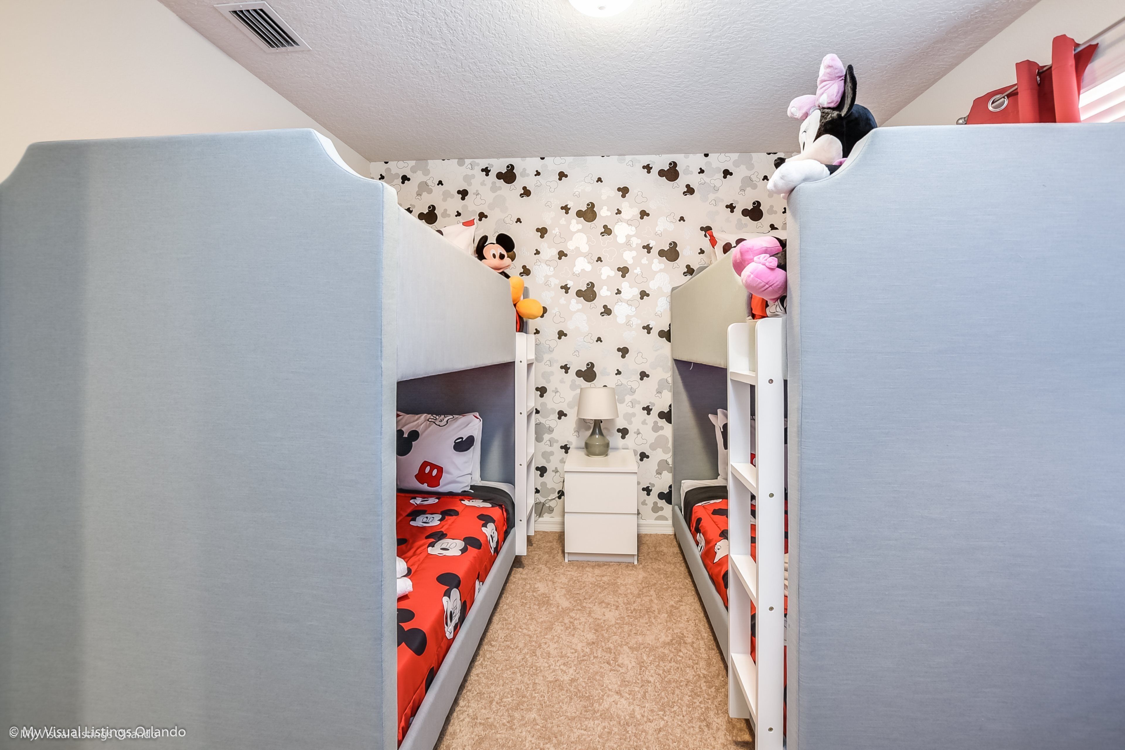 A children's bedroom with bunk beds, a small white nightstand, and a Mickey Mouse-themed wall.