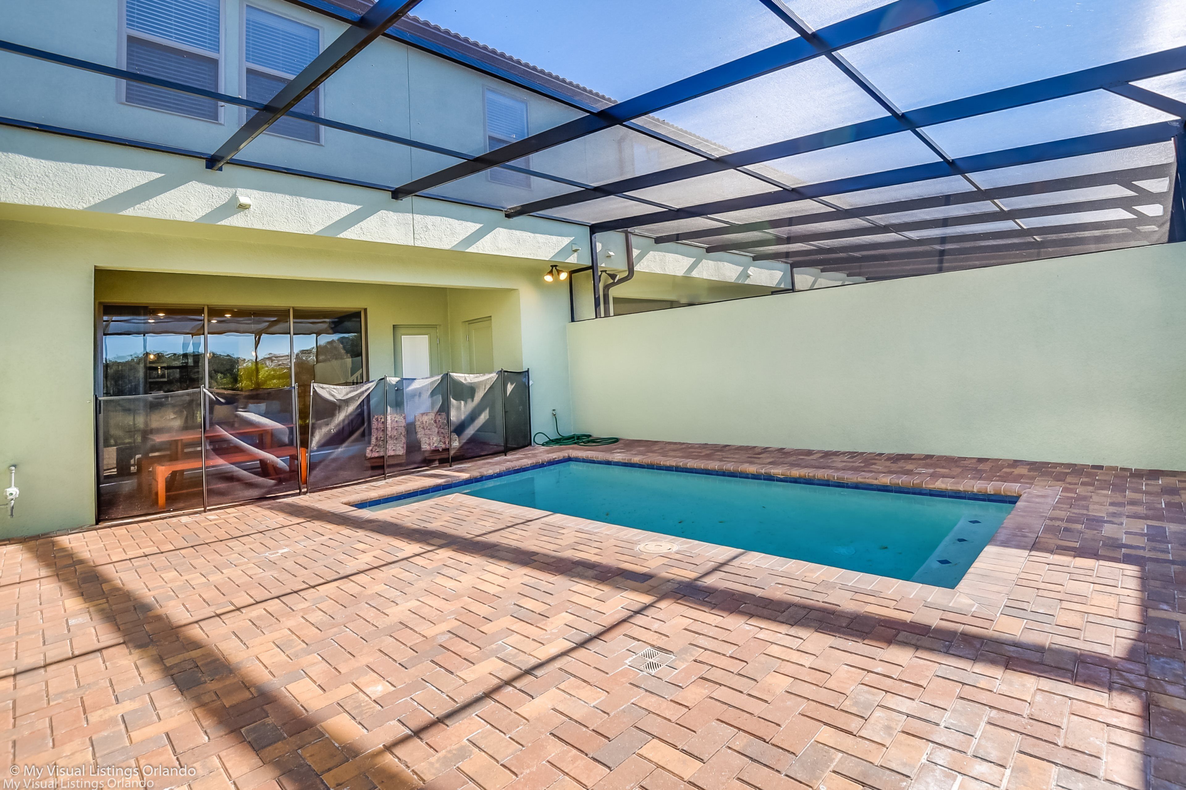 A swimming pool with a brick patio, a glass enclosure, and a view of the surrounding area.