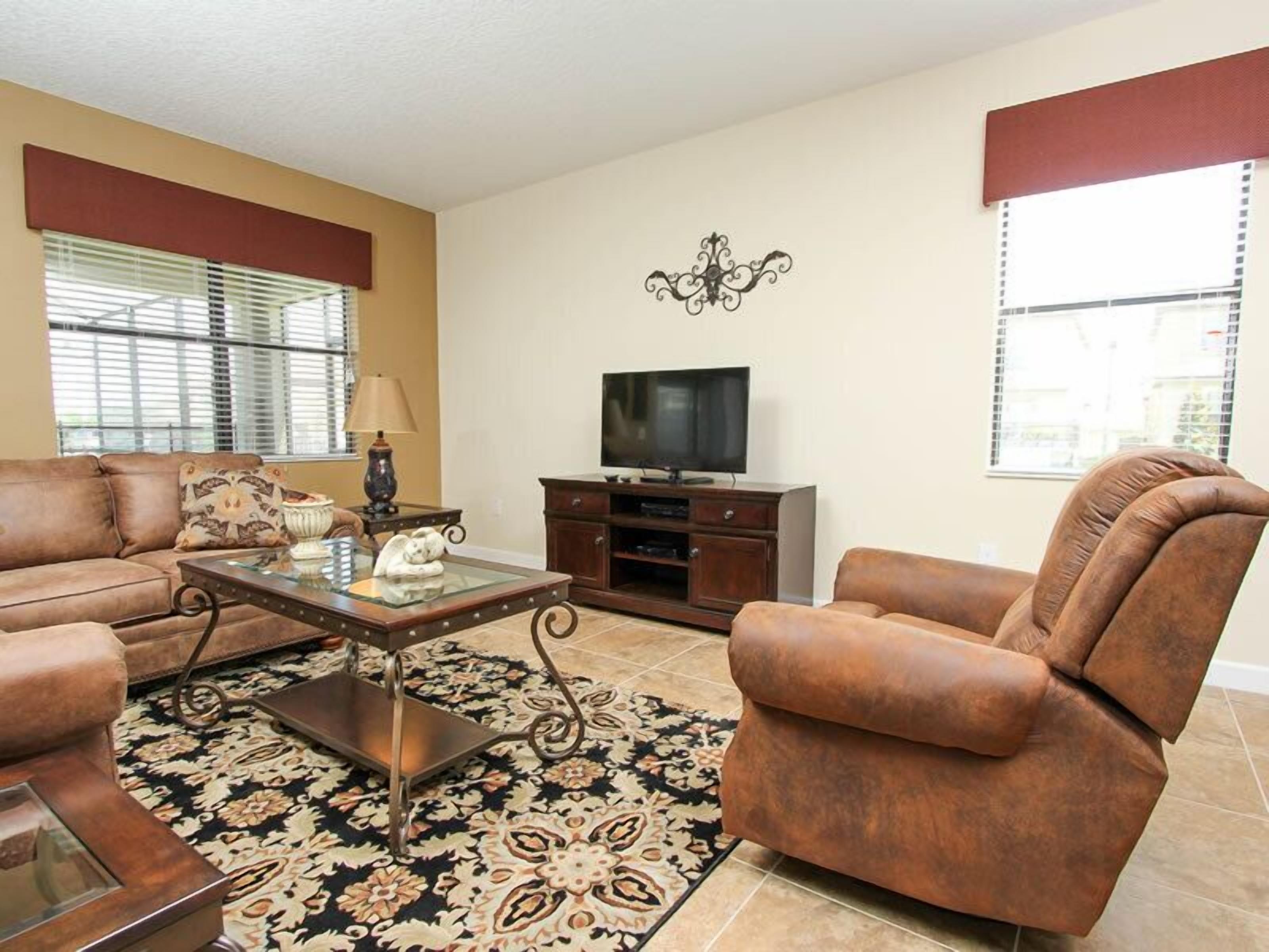 A living room with a sofa, armchair, TV stand, and decorative items.