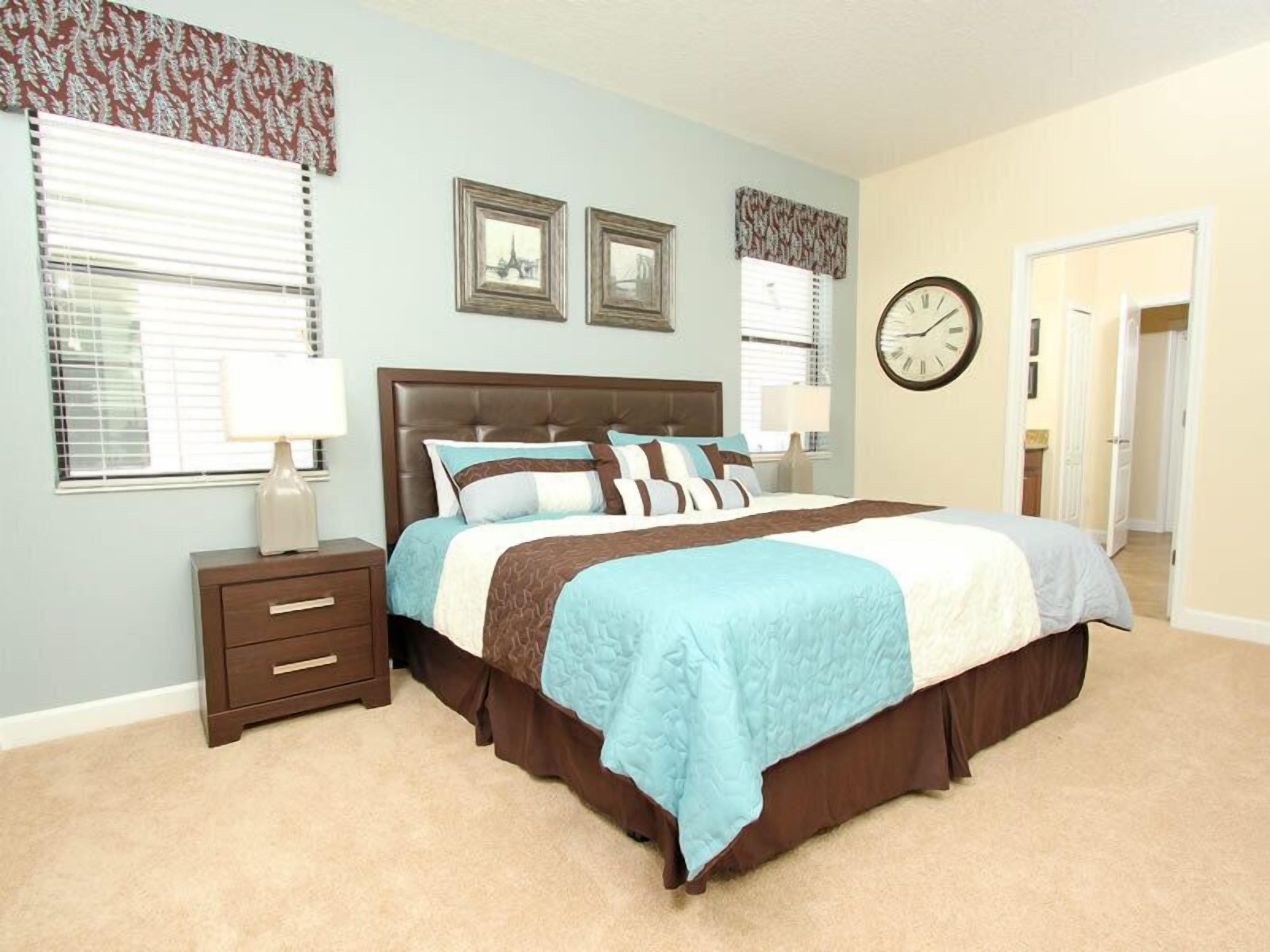 A bedroom with a large bed, two bedside tables, a nightstand, and a wall clock.