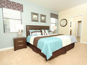 A bedroom with a large bed, two bedside tables, a nightstand, and a wall clock.