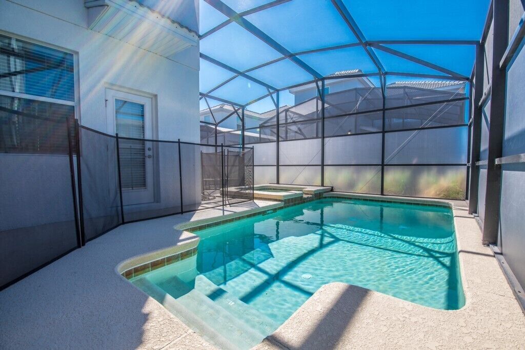A swimming pool with a glass enclosure, surrounded by a white wall and a door.