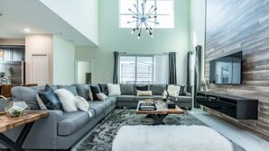 A modern living room with a grey sofa, a wooden coffee table, and a white fur ottoman. - 5 Bedroom Resort Villa with Game Room & Pool (Kissimmee)