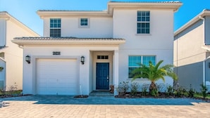 A two-story house with a garage, a front door, and a small garden with a palm tree. - 5 Bedroom Resort Villa with Game Room & Pool (Kissimmee)