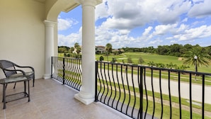 A balcony with a view of a golf course, a chair, and a railing. - Reunion Resort IHR 4070 (Kissimmee)