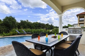 An outdoor patio with a pool, wicker chairs, a table with colorful glasses, and a grill. - Reunion Resort IHR 4070 (Kissimmee)
