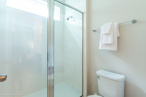 A bathroom with a glass shower enclosure, a white toilet, and a towel rack with folded towels.