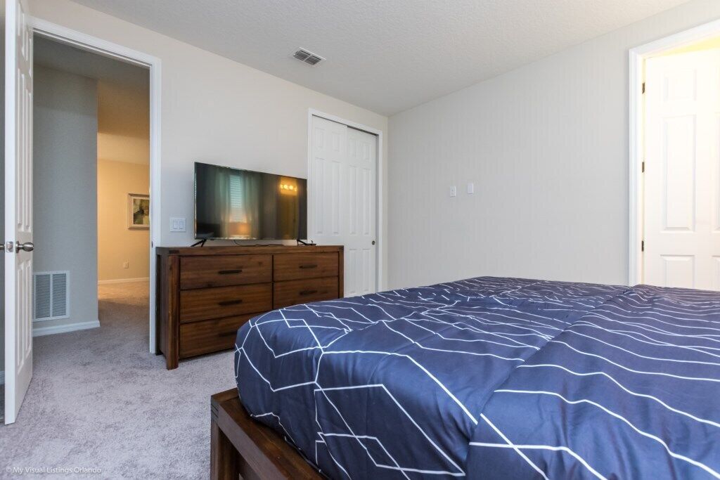 A bedroom with a bed, a dresser, a television, and a door.