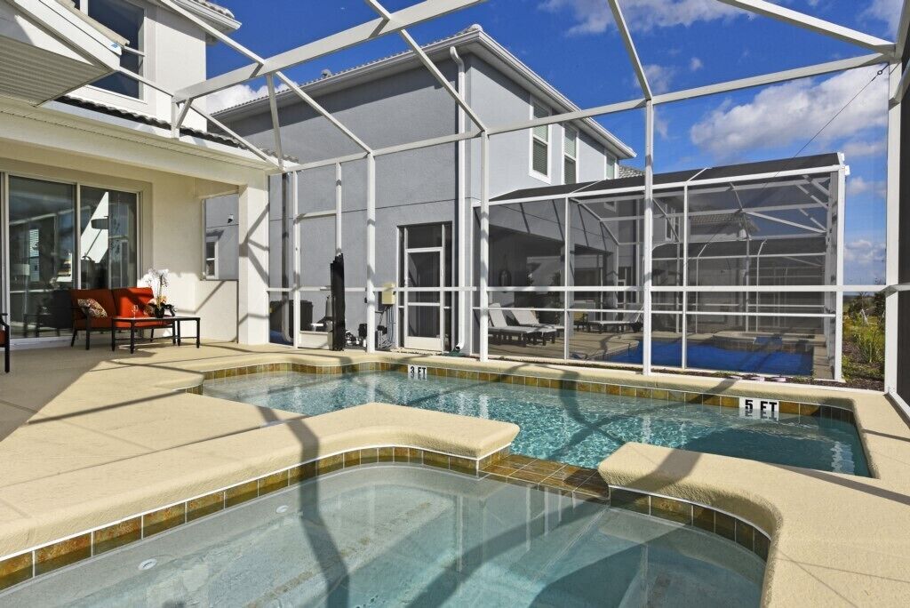 A swimming pool with a glass enclosure, lounge chairs, and a patio area.