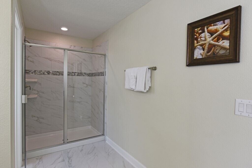 A bathroom with a glass shower enclosure, a marble-tiled floor, and a framed picture on the wall.