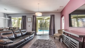 A modern living room with a leather sofa, a dining table, and a large window with curtains. - Emerald Island - IHR 4067 (Kissimmee)
