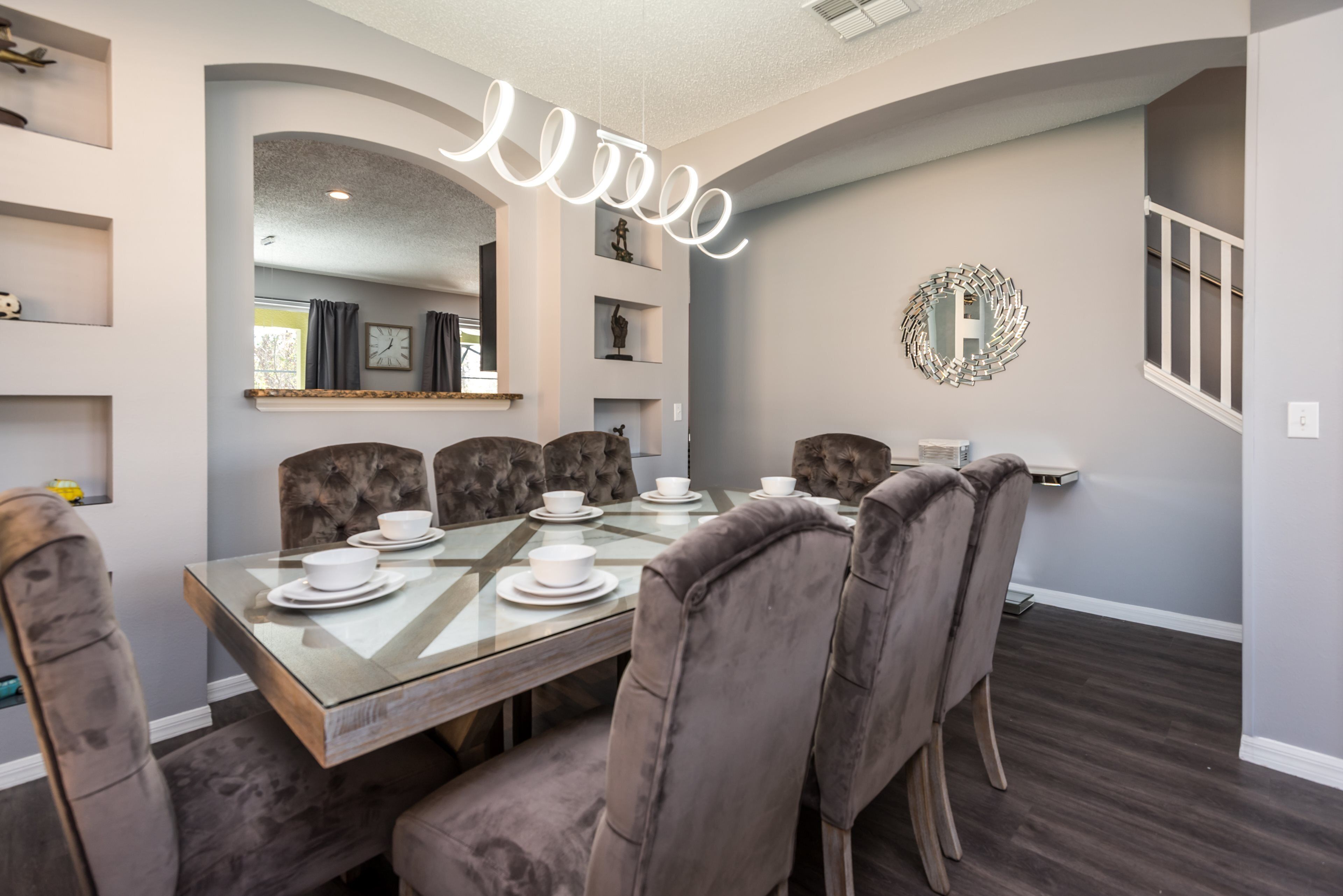 A dining area with a glass table, cushioned chairs, and a decorative mirror on the wall.