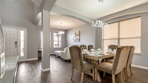 A dining area with a wooden table, beige upholstered chairs, and a modern pendant light. - Emerald Island - IHR 4067 (Kissimmee)