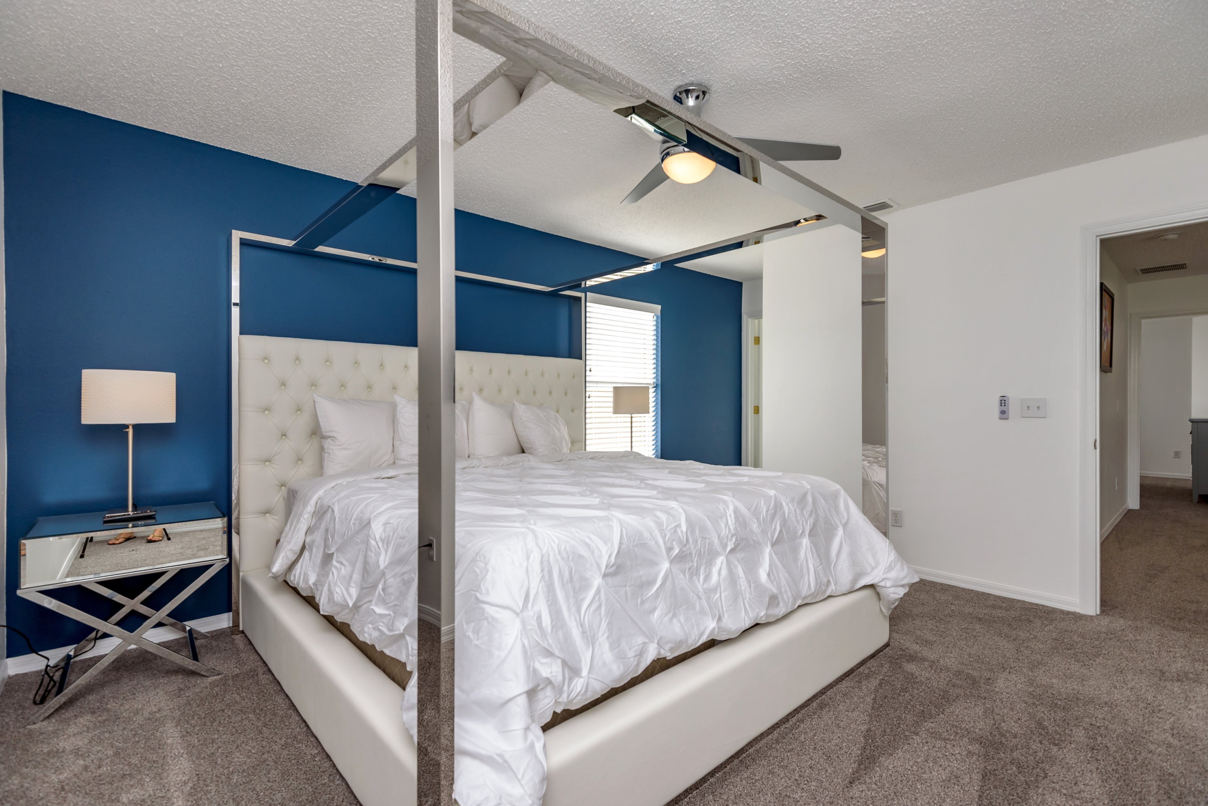 Ein Schlafzimmer mit einem weißen Bett, einem Nachttisch, einer Lampe und einem Deckenventilator.