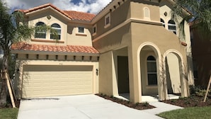 Une maison à deux étages, avec une façade beige, un toit recouvert de tuiles rouges et un garage.