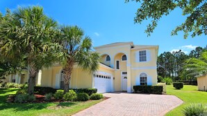 A two-story house with a driveway, palm trees, and a well-maintained lawn.