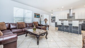 A modern living room with a brown leather sofa, a marble coffee table, and a kitchen area with white cabinets and a stone backsplash.