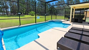 A covered swimming pool with a patio area, surrounded by a fence and trees.