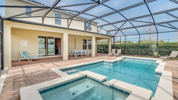 A covered outdoor swimming pool with a patio area, lounge chairs, and a table. - 1210yc (Davenport)