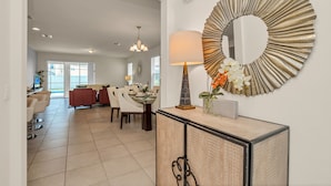 A modern living room with a dining area, a large decorative mirror, and a lamp with flowers. - 1210yc (Davenport)