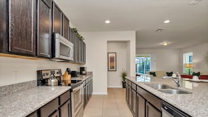 A modern kitchen with dark wood cabinets, granite countertops, stainless steel appliances, and a central island with a sink. - 1210yc (Davenport)