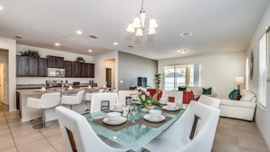 A modern kitchen with dark cabinets, a central island, and a dining area with white chairs and a glass-top table. - 1210yc (Davenport)
