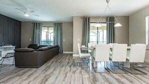 Un salon moderne comprenant un canapé, une table à manger et des chaises, un ventilateur de plafond et de grandes fenêtres avec des rideaux.