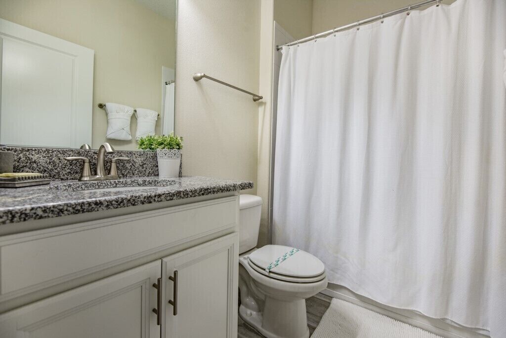 A bathroom with a white toilet, a granite countertop, a white sink, and a shower curtain.
