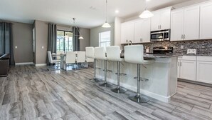 Une cuisine moderne avec des meubles blancs, un plan de travail en granit et un îlot central doté de tabourets de bar.