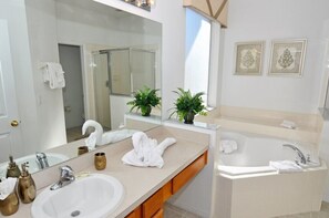 A modern bathroom with two sinks, a large mirror, a bathtub, and decorative plants. - Terra Verde IHR 3063 (Kissimmee)