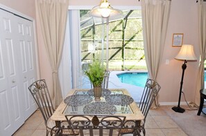 A dining area with a glass table, metal chairs, a vase with plants, a pool view, and a lamp. - Terra Verde IHR 3063 (Kissimmee)