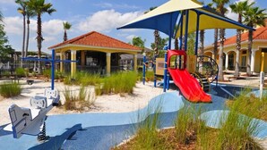 A playground with a red slide, a blue and yellow canopy, and a small building with a red roof. - Terra Verde IHR 3063 (Kissimmee)
