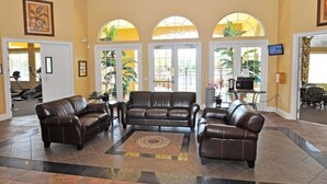 A spacious lobby with a brown leather sofa set, a patterned rug, and large arched windows with plants. - Terra Verde IHR 3063 (Kissimmee)