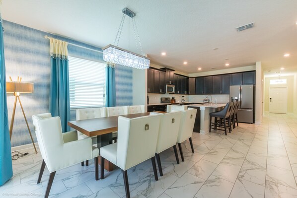 A modern kitchen with dark cabinets, a central island, and a dining area with white chairs and a wooden table.