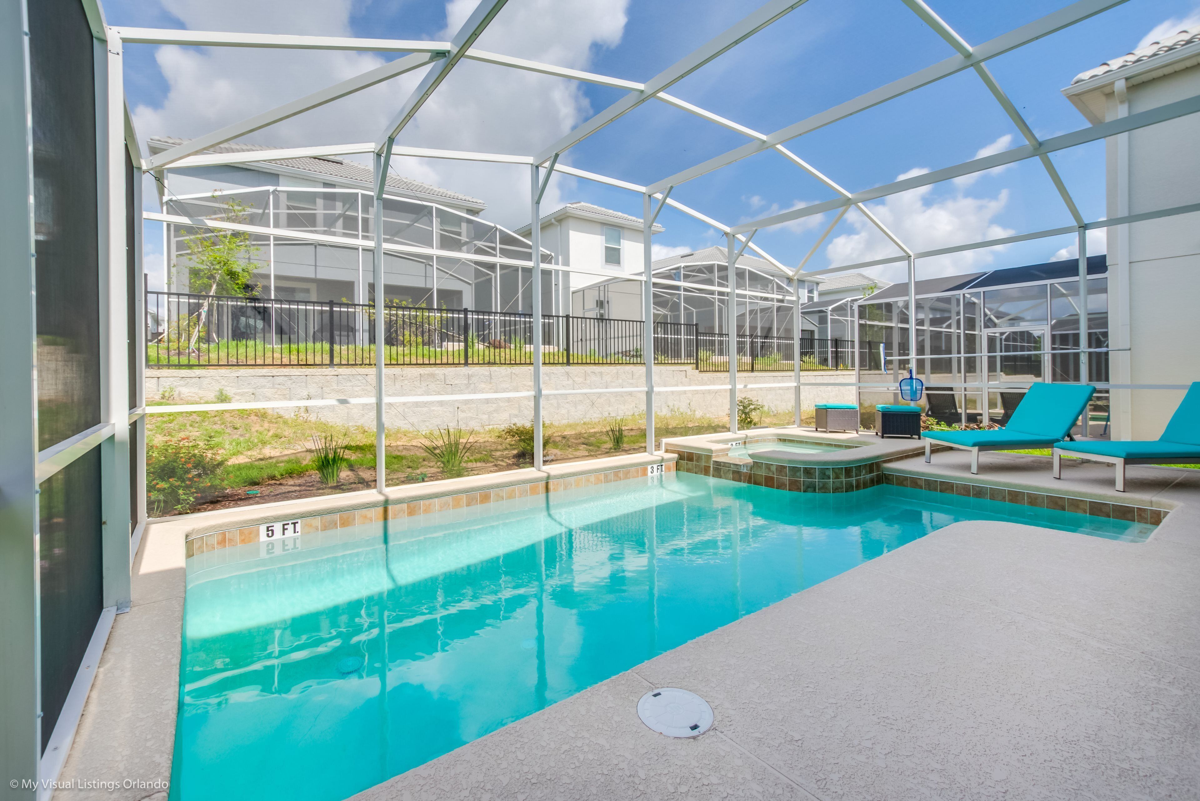 Un área de piscina con cerramiento de vidrio, sillas de descanso y un jacuzzi.