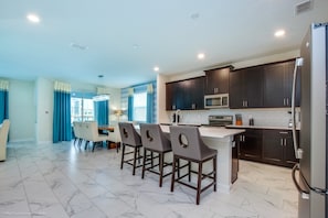 A modern kitchen with dark cabinets, a stainless steel refrigerator, and a marble-tiled floor.