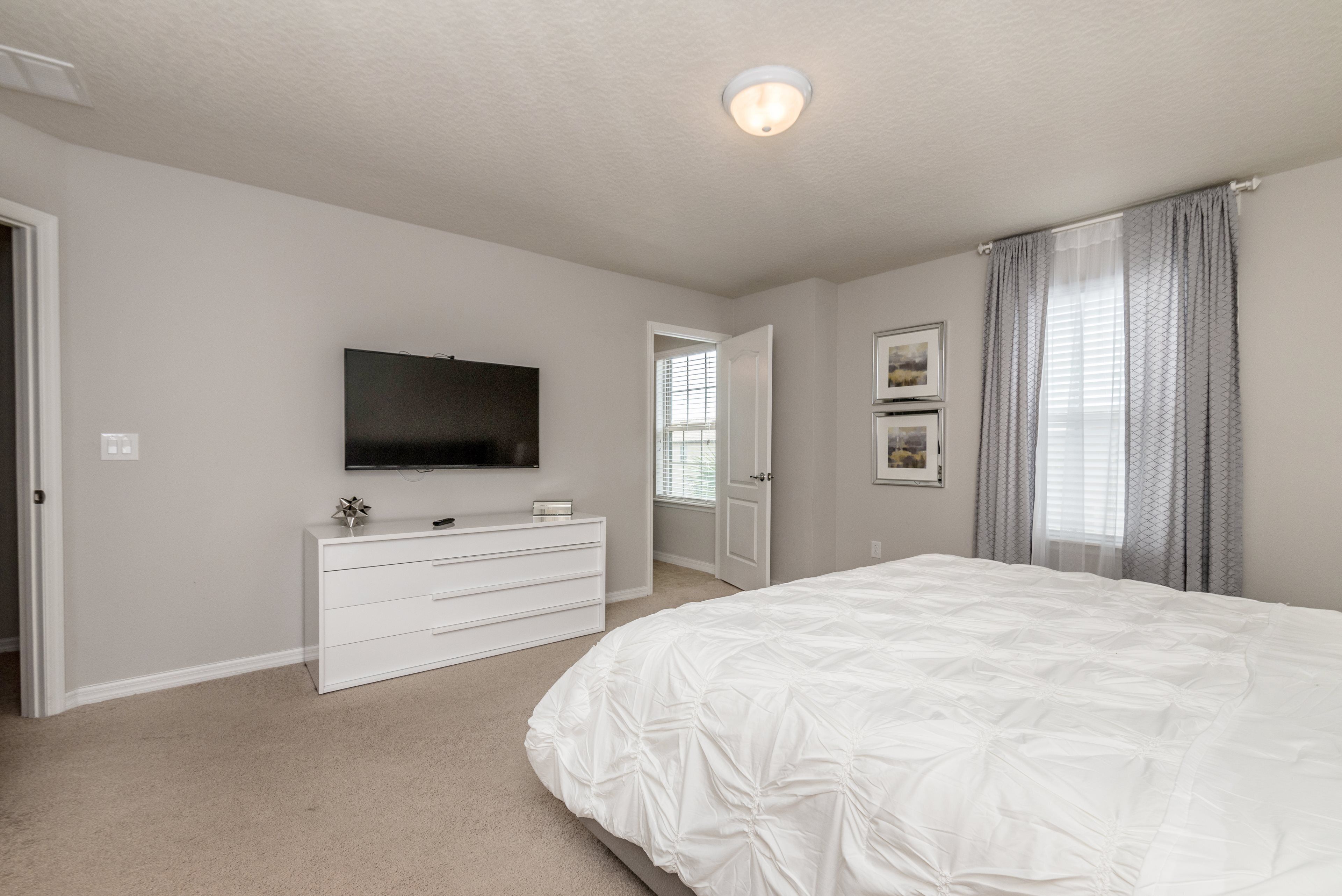A bedroom with a large bed, a dresser, a television mounted on the wall, and a door leading to another room.