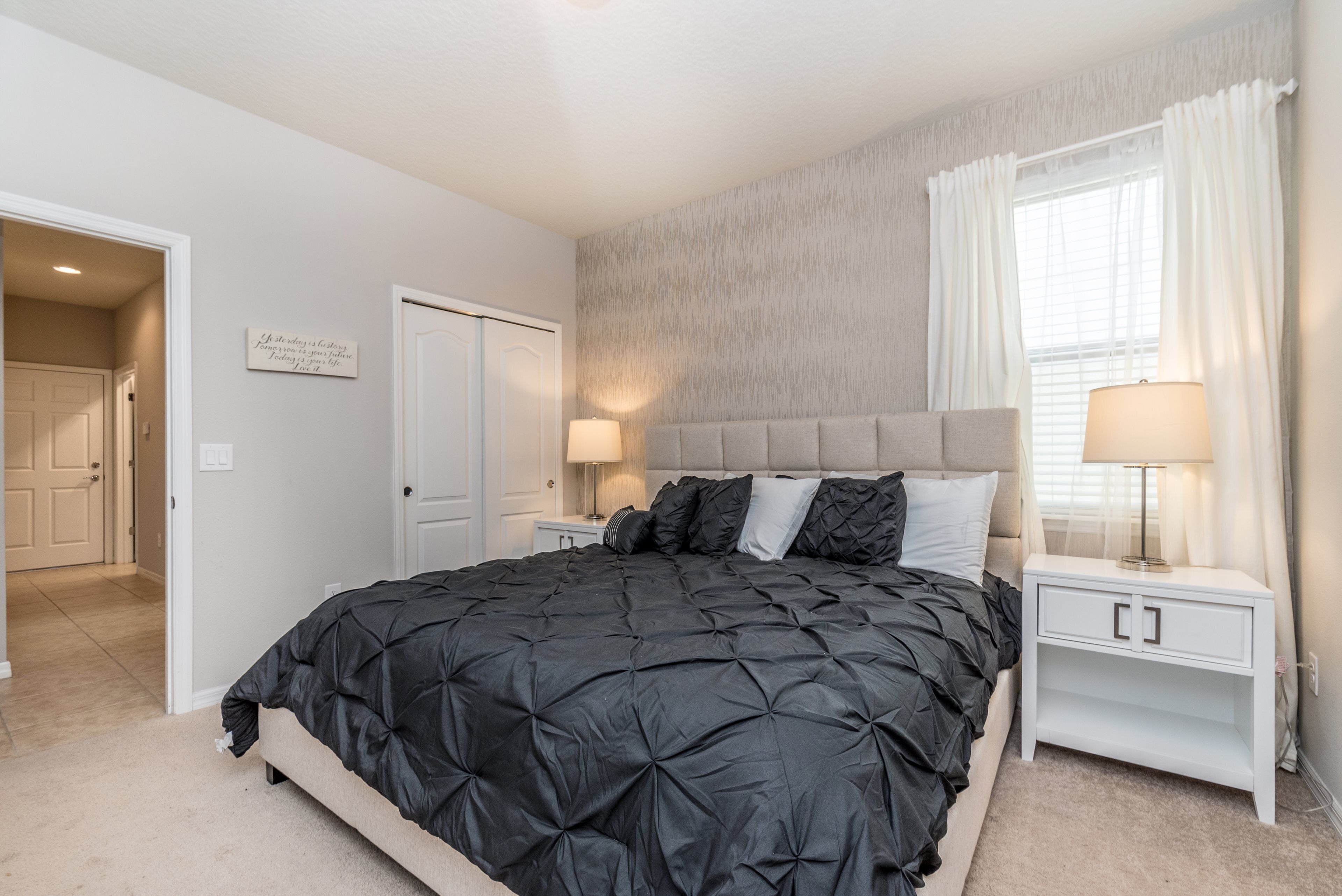 A bedroom with a large bed, a nightstand with a lamp, and a door leading to another room.