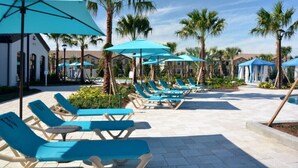 A poolside area with lounge chairs and umbrellas, surrounded by palm trees and buildings. - 2105mw Luxury 6 Bed Villa With Pool & Spa (Kissimmee)