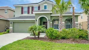 A two-story house with a green garage, a front porch, and a landscaped front yard with palm trees and shrubs. - 5 Bedroom, 4 Bathroom Villa (Davenport)