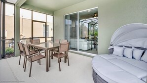 A sunlit patio with a dining table and chairs, a covered bed, and a sliding glass door leading to a backyard. - 5 Bedroom, 4 Bathroom Villa (Davenport)