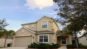 A two-story house with a beige exterior, a garage, and a front yard with landscaping. - 207bon (Davenport)
