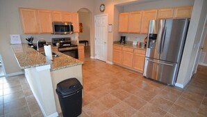 A kitchen with granite countertops, stainless steel appliances, wooden cabinets, and a black trash bin. - 207bon (Davenport)