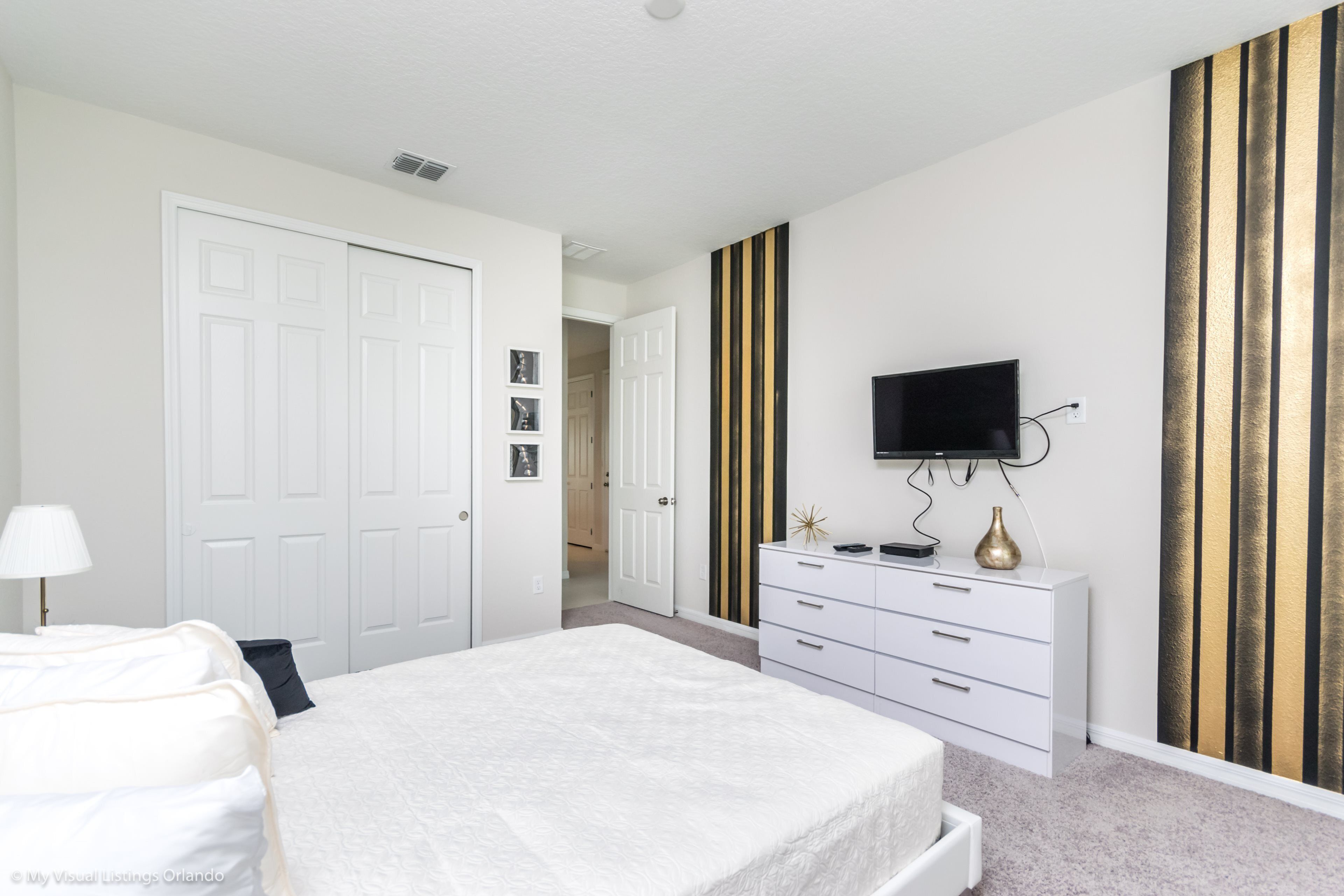 Een slaapkamer met een bed, een dressoir, een televisie en een deur.