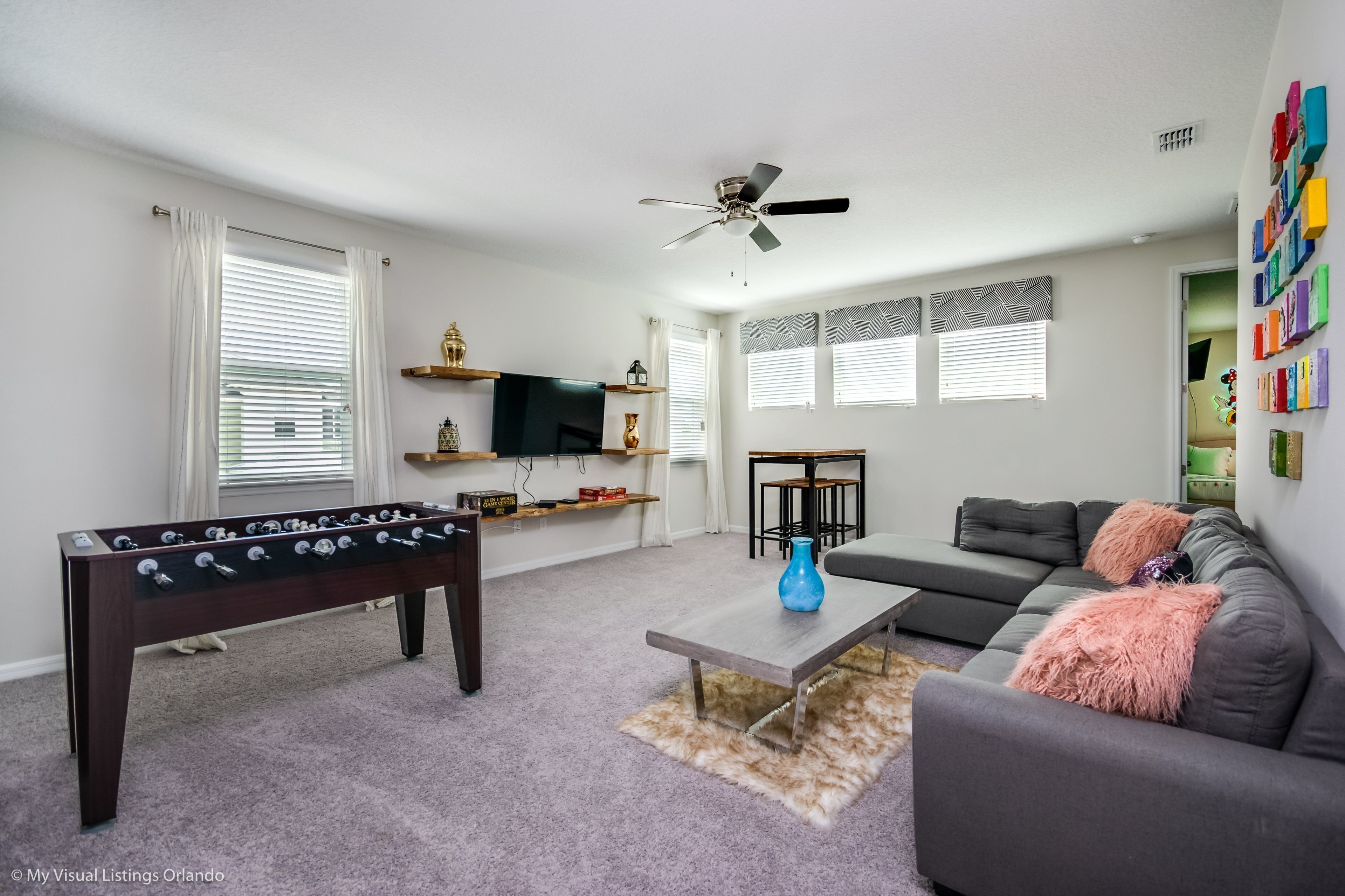 A living room with a foosball table, a grey sofa, a coffee table, and a ceiling fan.
