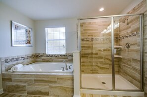 A bathroom with a large bathtub, a shower with glass doors, and a window with blinds.