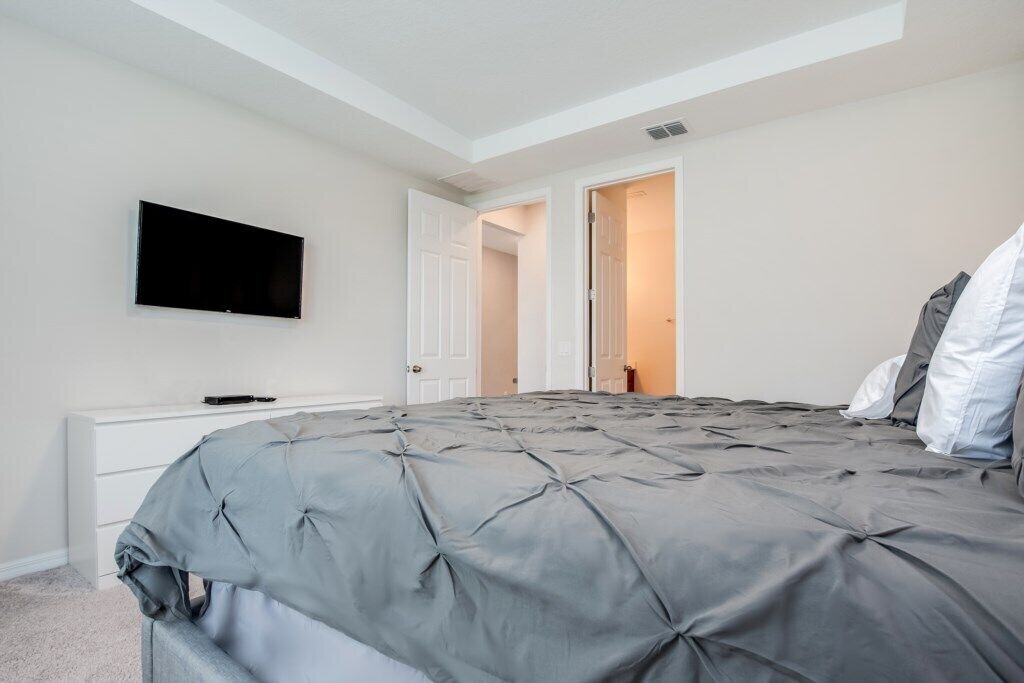 Quarto com cama grande, TV de tela plana fixada na parede e porta para outro cômodo.