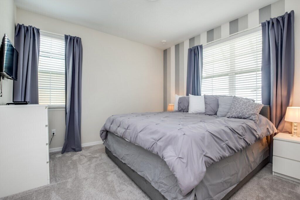 Un dormitorio con cama, cortinas, televisor y mesita de noche.